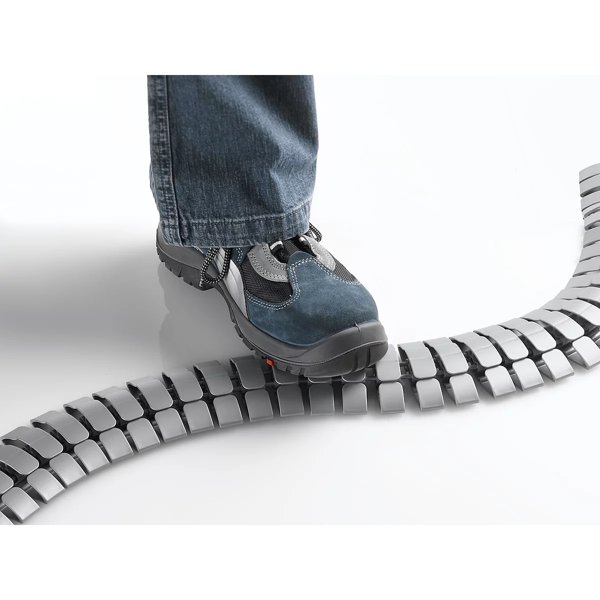 A foot in jeans and safety shoe stands on a gray cable duct.