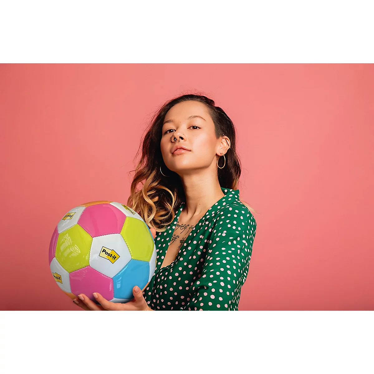 Une jeune femme en robe verte à pois blancs tient un ballon coloré. Elle regarde l'appareil photo.