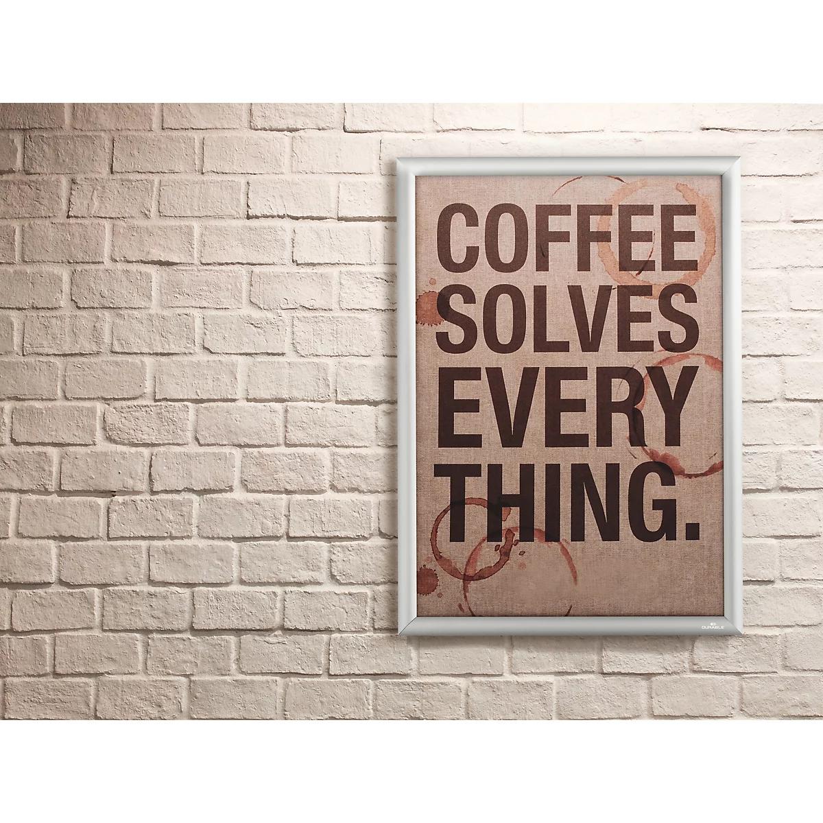 Affiche dans un cadre argenté sur un mur en briques blanches avec le texte Coffee solves everything et des taches de café.