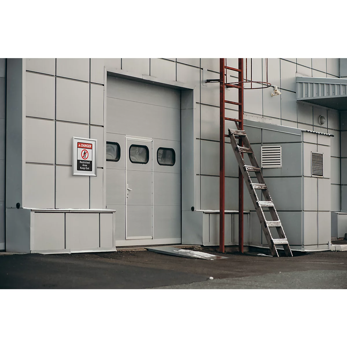 Bâtiment industriel avec porte sectionnelle et échelle appuyée contre la façade.