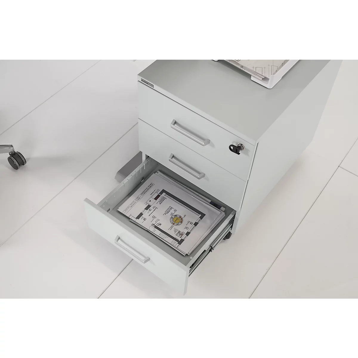 Caisson roulant gris clair, un tiroir ouvert. Des papiers avec des dessins sont à l'intérieur.