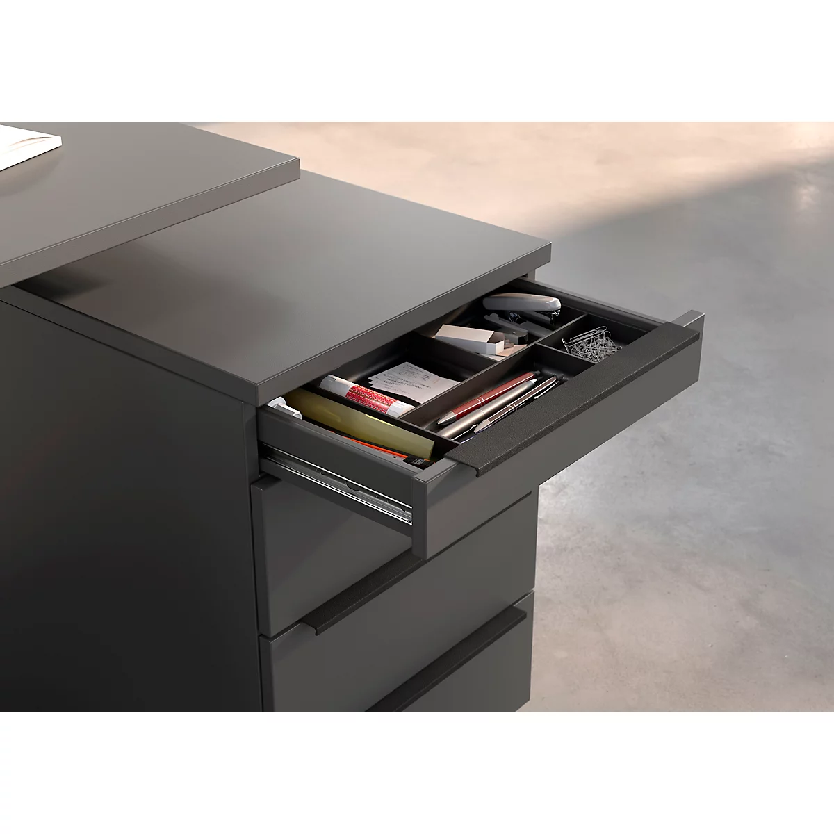 Bureau gris avec tiroir ouvert, rempli de fournitures de bureau.