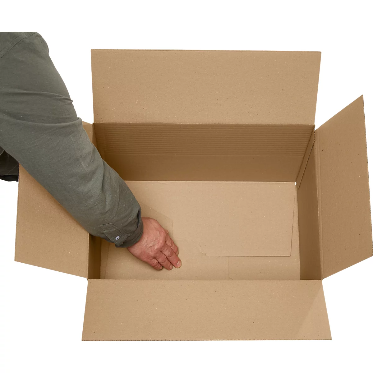 Una mano de una persona alcanza una caja de cartón marrón abierta. Las paredes de la caja son de cartón corrugado.