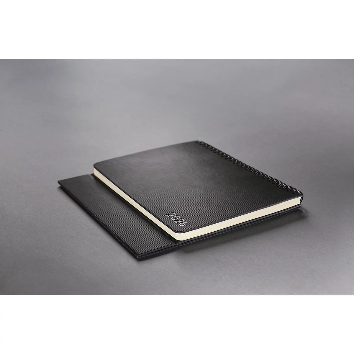Cahier noir avec l'empreinte '2026'. Il repose sur un autre cahier sur fond gris.