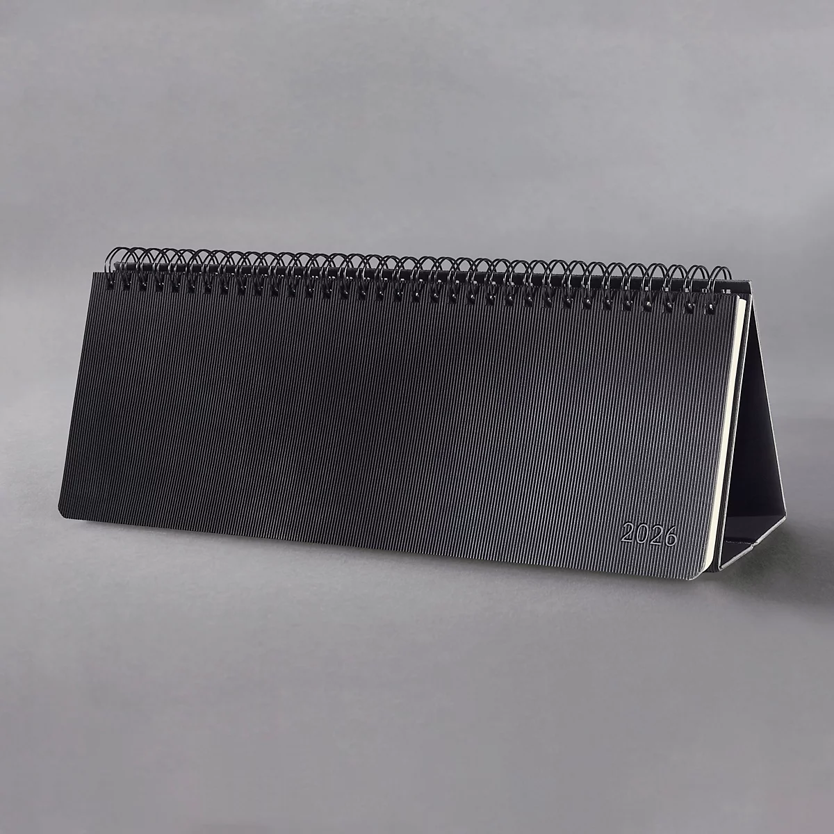 Calendrier de bureau noir avec reliure spirale, fond gris. Impression "2026".