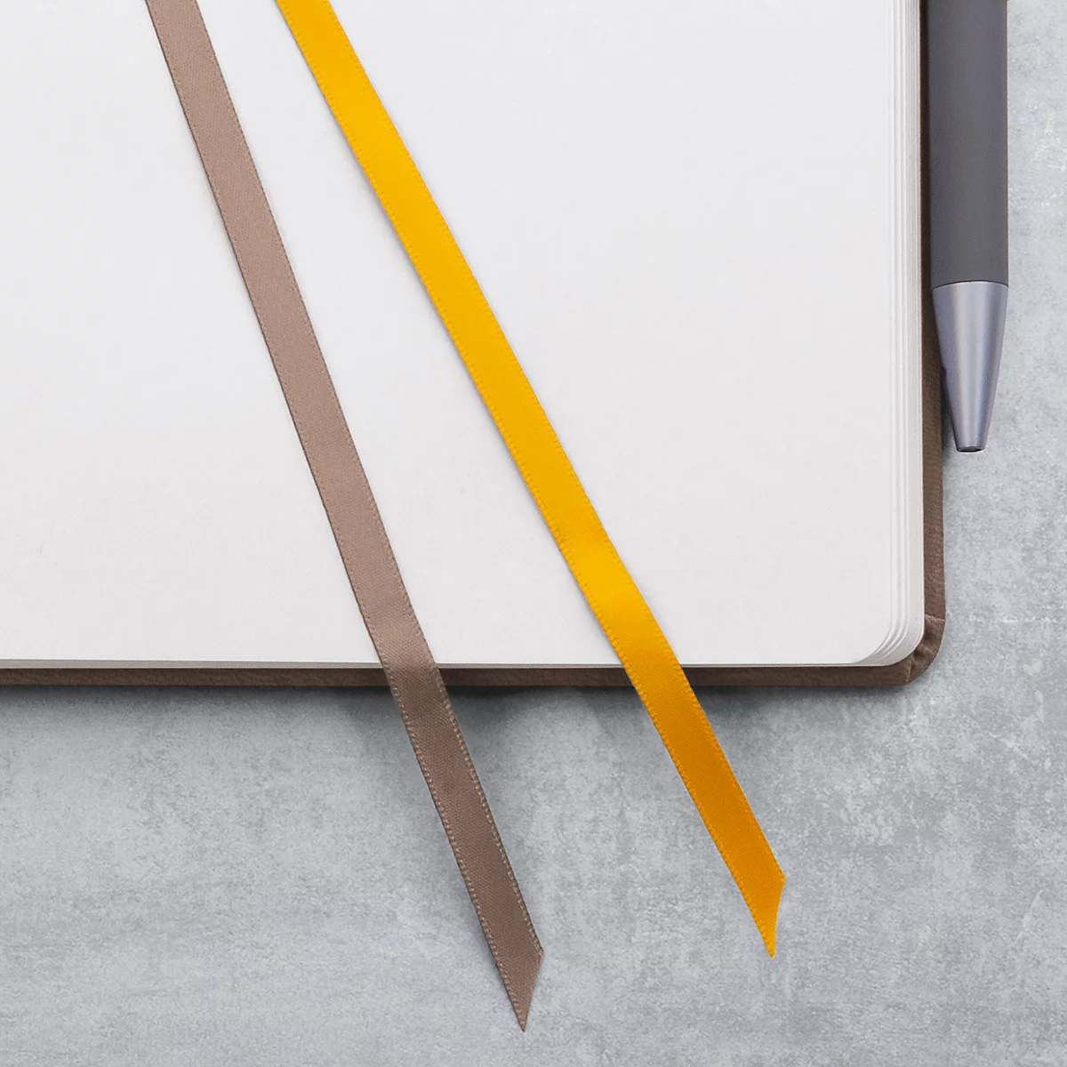 Carnet avec couverture marron et deux marque-pages colorés, jaune et marron. À côté, un stylo.