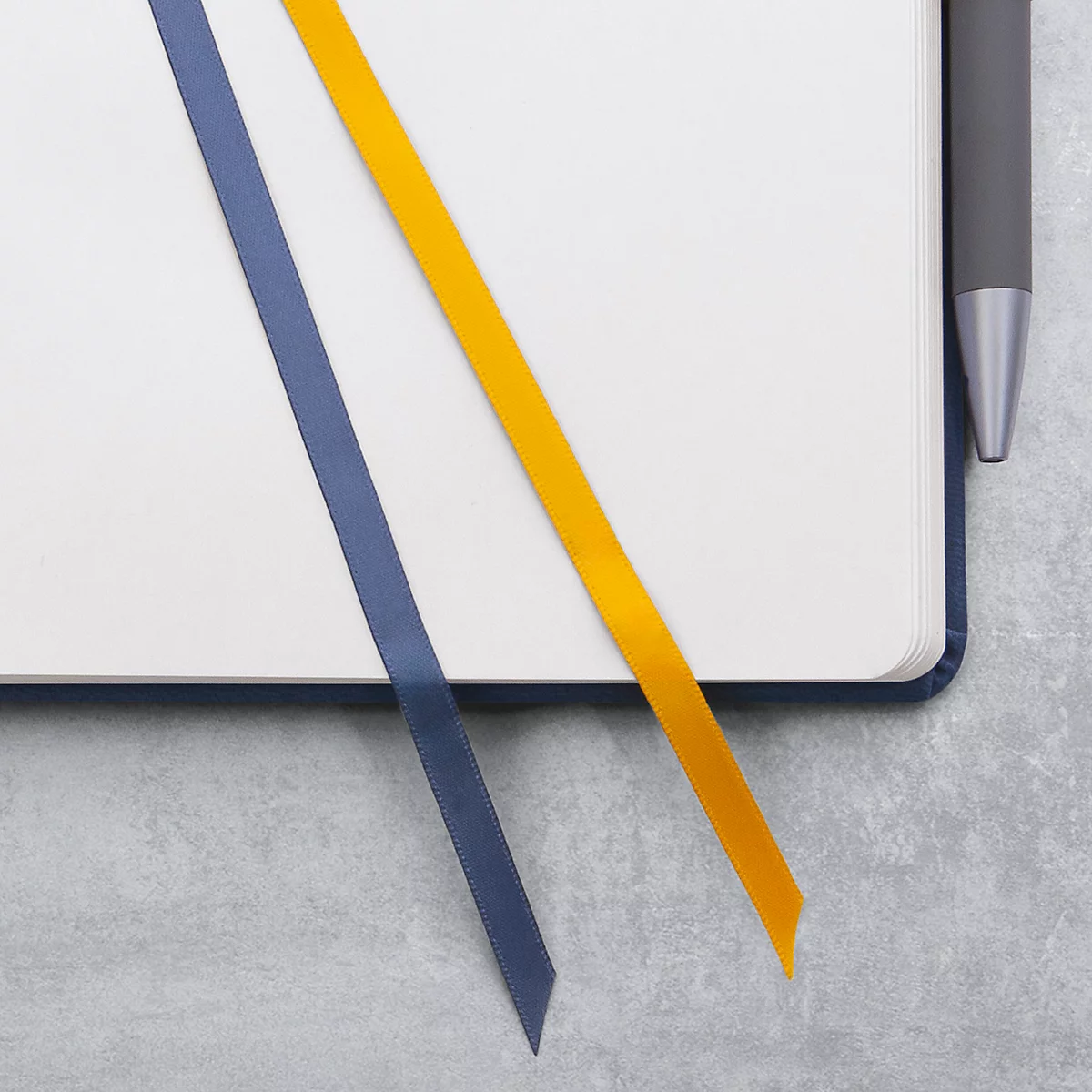 Carnet avec marque-page bleu et jaune, à côté d'un stylo.
