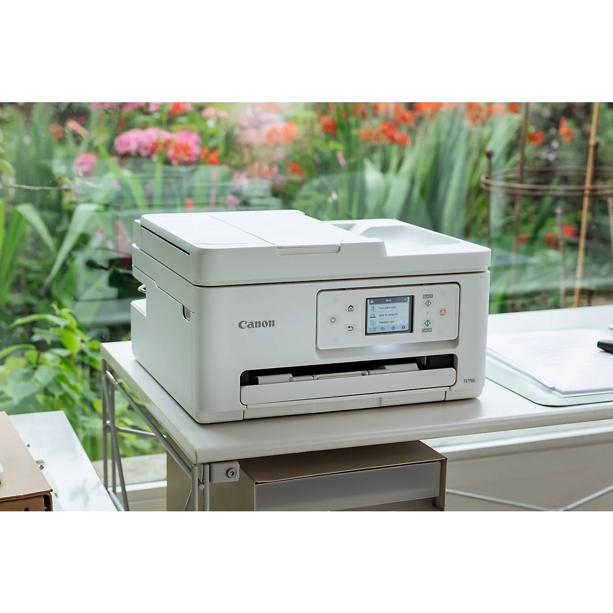 Ein weißer Canon-Multifunktionsdrucker steht auf einem Schreibtisch vor einem unscharfen Gartenhintergrund.