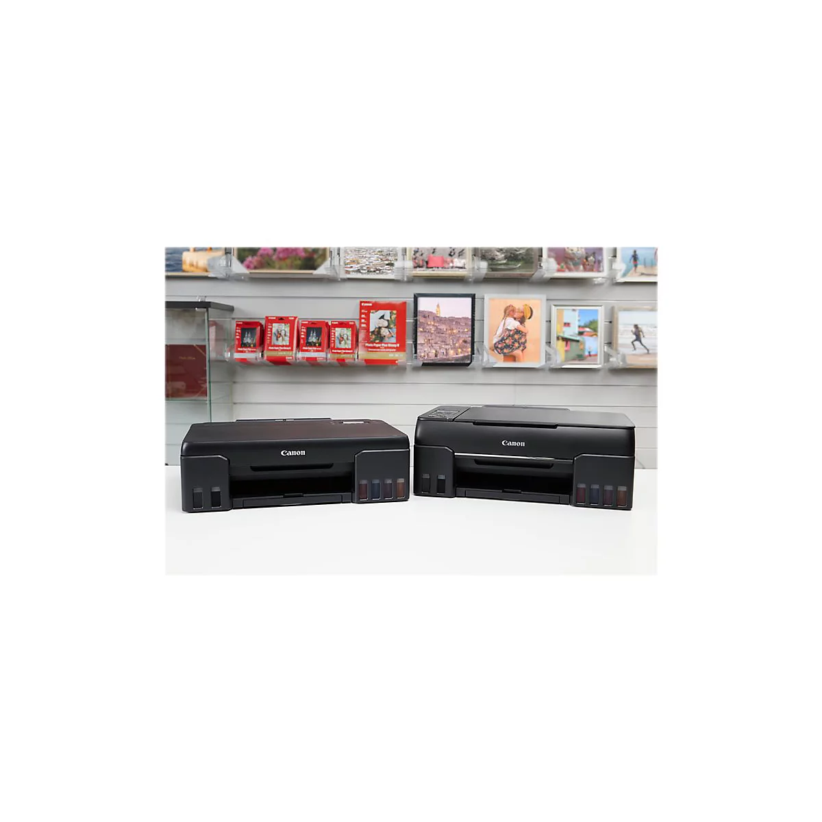 Zwei schwarze Canon-Drucker stehen nebeneinander. Im Hintergrund sind Fotos und Bilder ausgestellt.