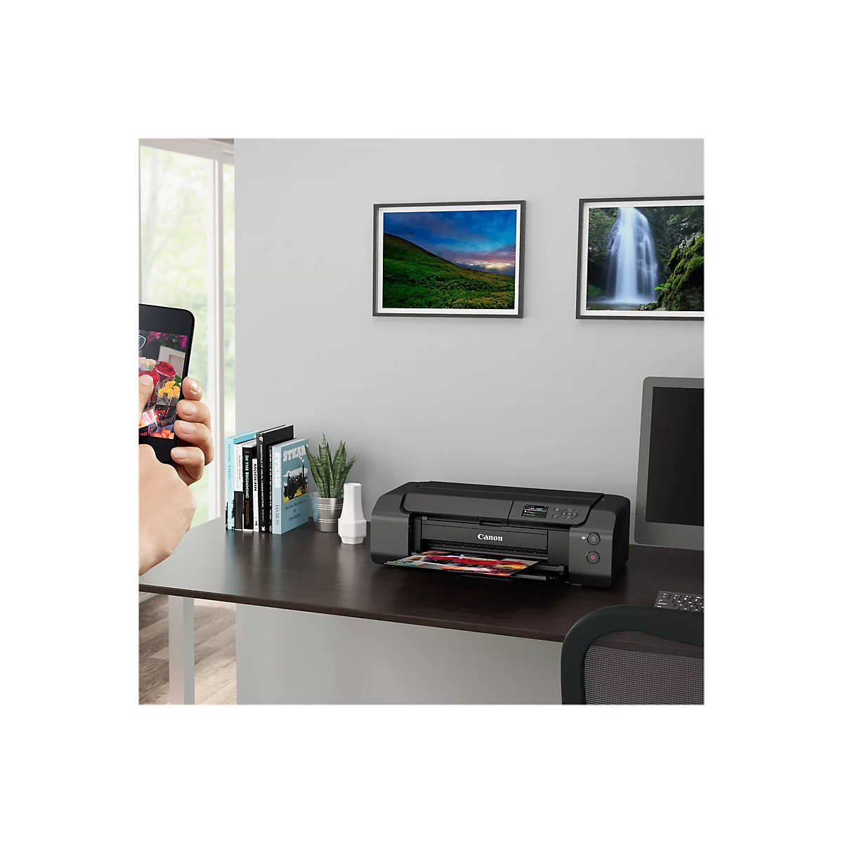 Ein Drucker steht auf einem Schreibtisch. Auf dem Display werden Bilder angezeigt, daneben liegt ein Smartphone mit einem Blumenstrauß-Foto.