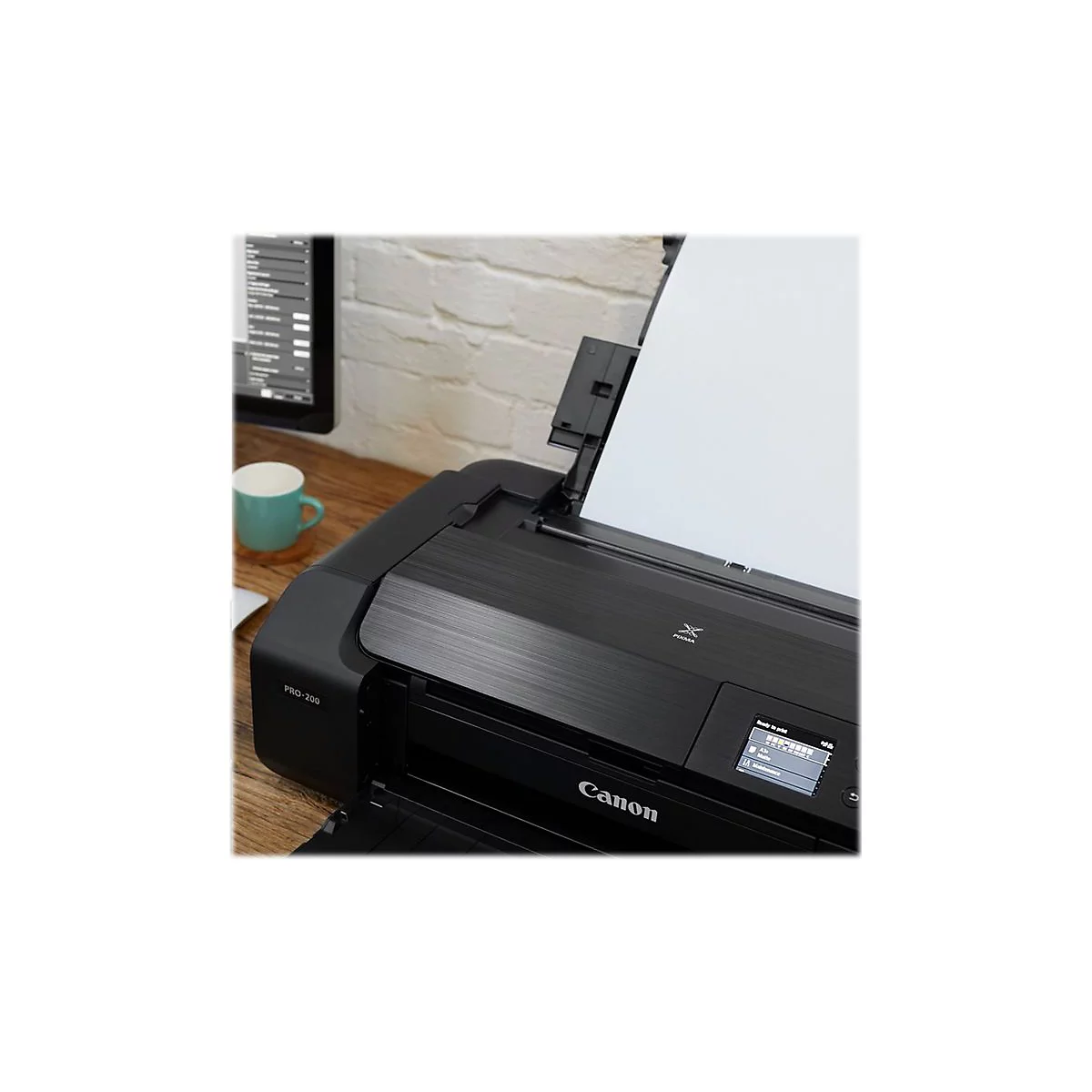 Schwarzer Canon-Drucker mit Papierauswurf. Auf dem Bedienfeld steht "Ready to print". Im Hintergrund: Schreibtisch, Bildschirm, Tasse.