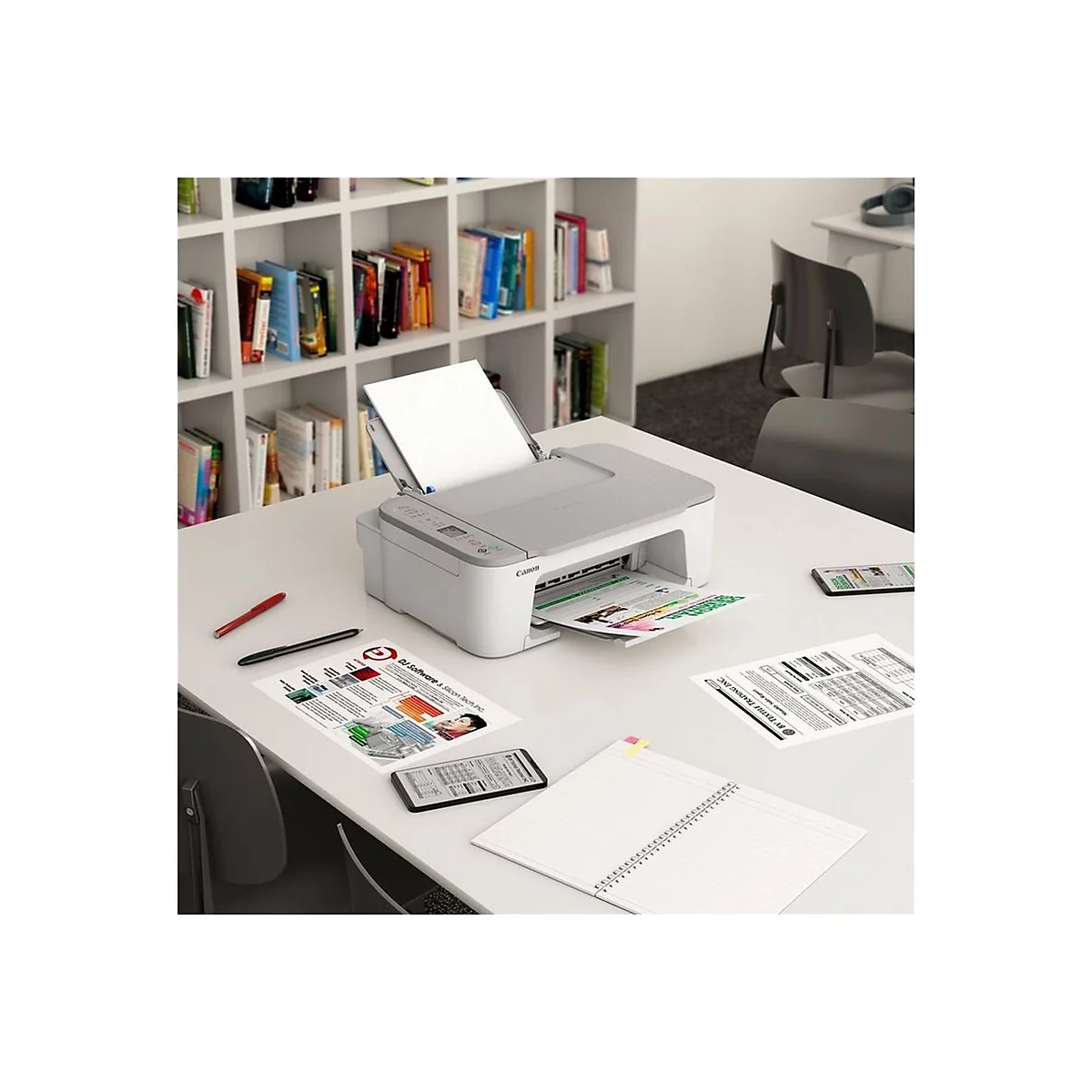 Ein weiÃŸer Drucker druckt Farbseiten auf einem Tisch, darauf liegen Notizblock, Smartphone, Stifte.