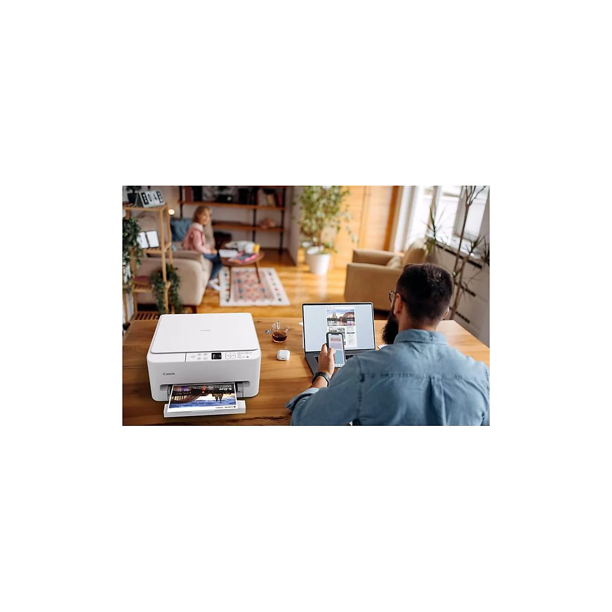 Mann druckt mit Canon-Drucker in hellem Wohnzimmer, im Hintergrund sitzt ein Kind.