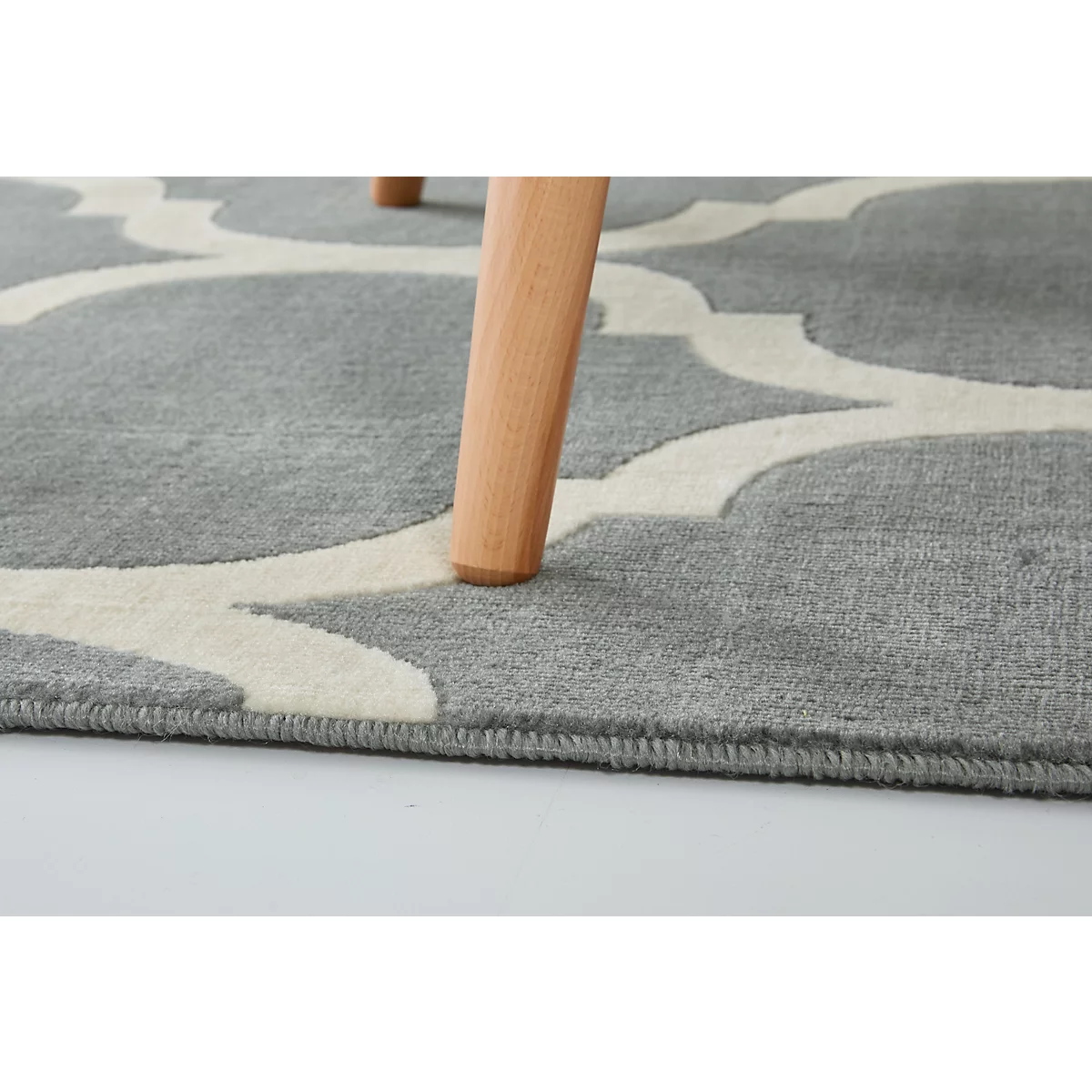 Gray carpet with white pattern, wooden leg, close-up.