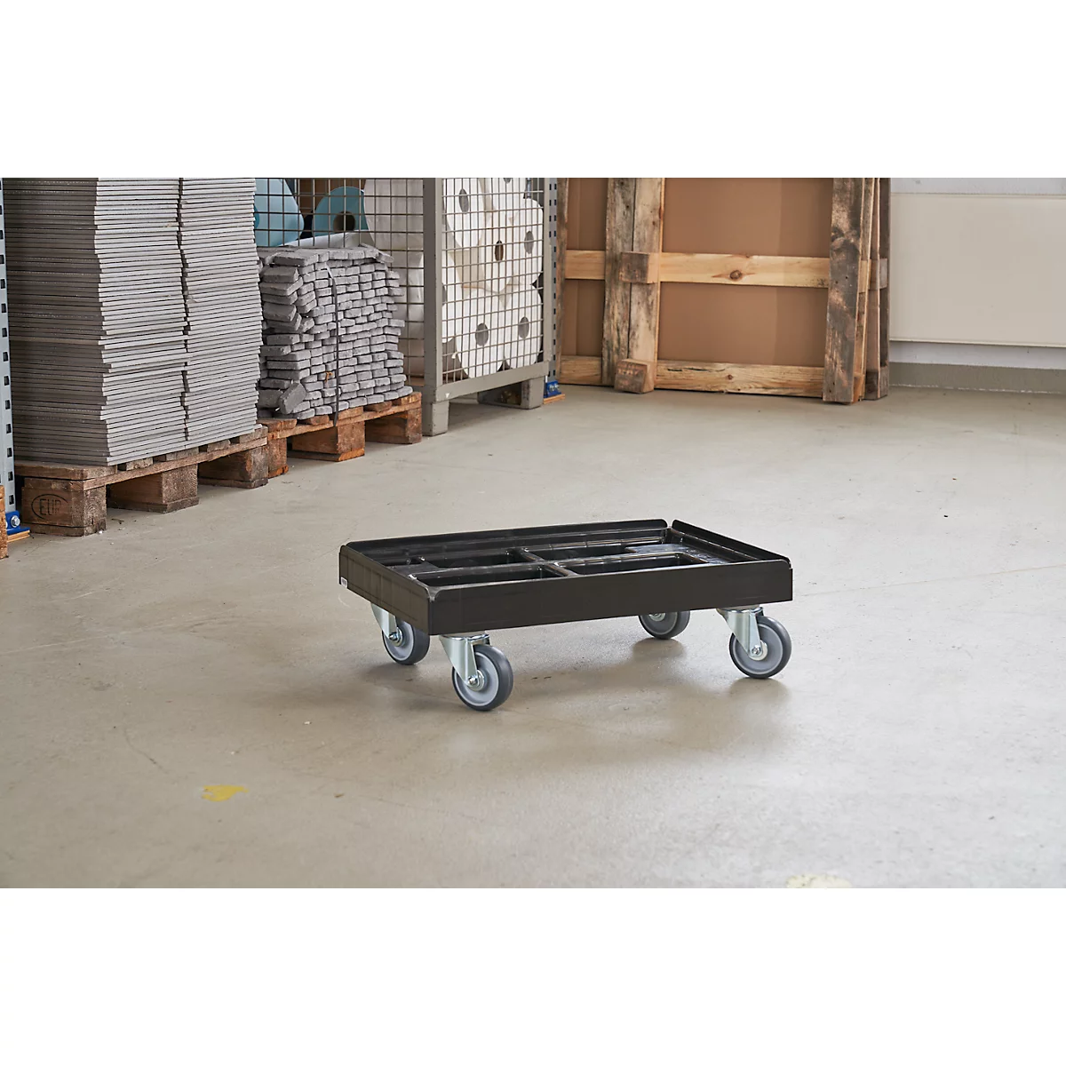 Carro de transporte negro sobre cuatro ruedas, en un almacén.