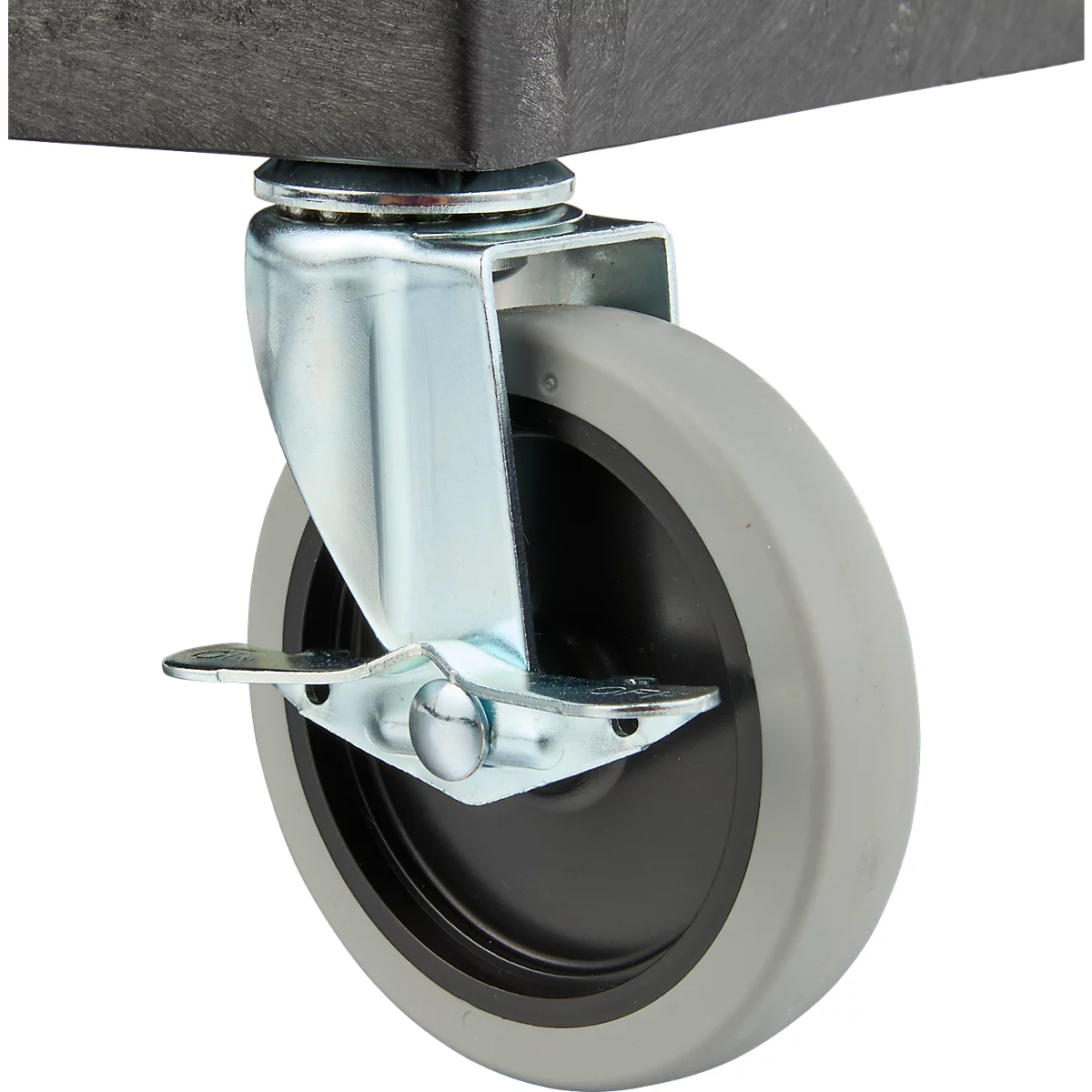 Primer plano de una rueda giratoria gris con freno, montada debajo de una pieza de plástico oscuro.