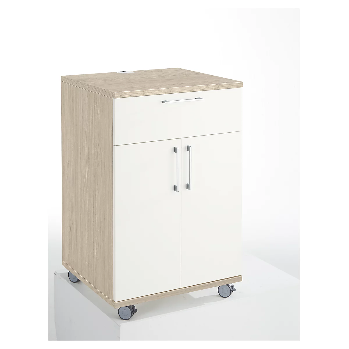 A white and beige cabinet on wheels with a drawer and double door. The cabinet stands on a white surface.