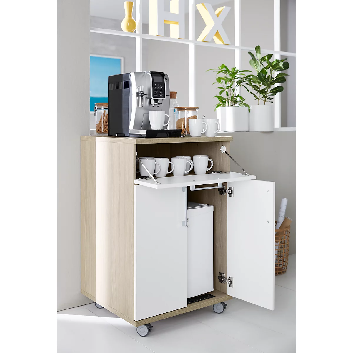 Coffee machine on a wooden cabinet with a fold-out door. White cups and plants decorate the furniture.