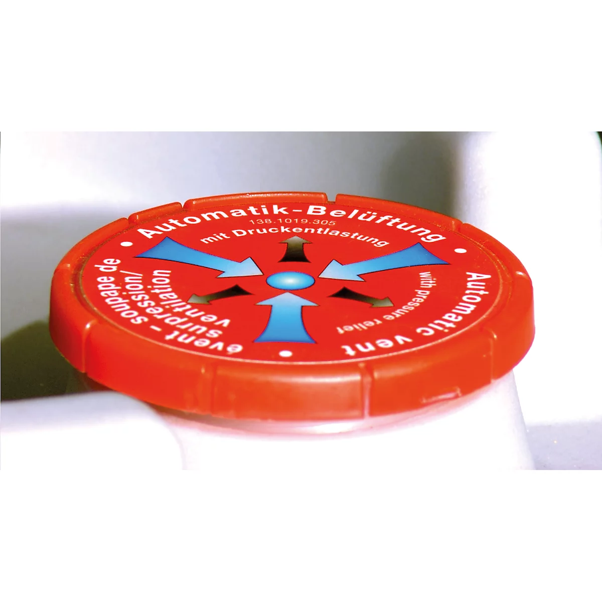 Red, round lid with text: "Automatik-Belüftung" and arrows. A white surface in the background.