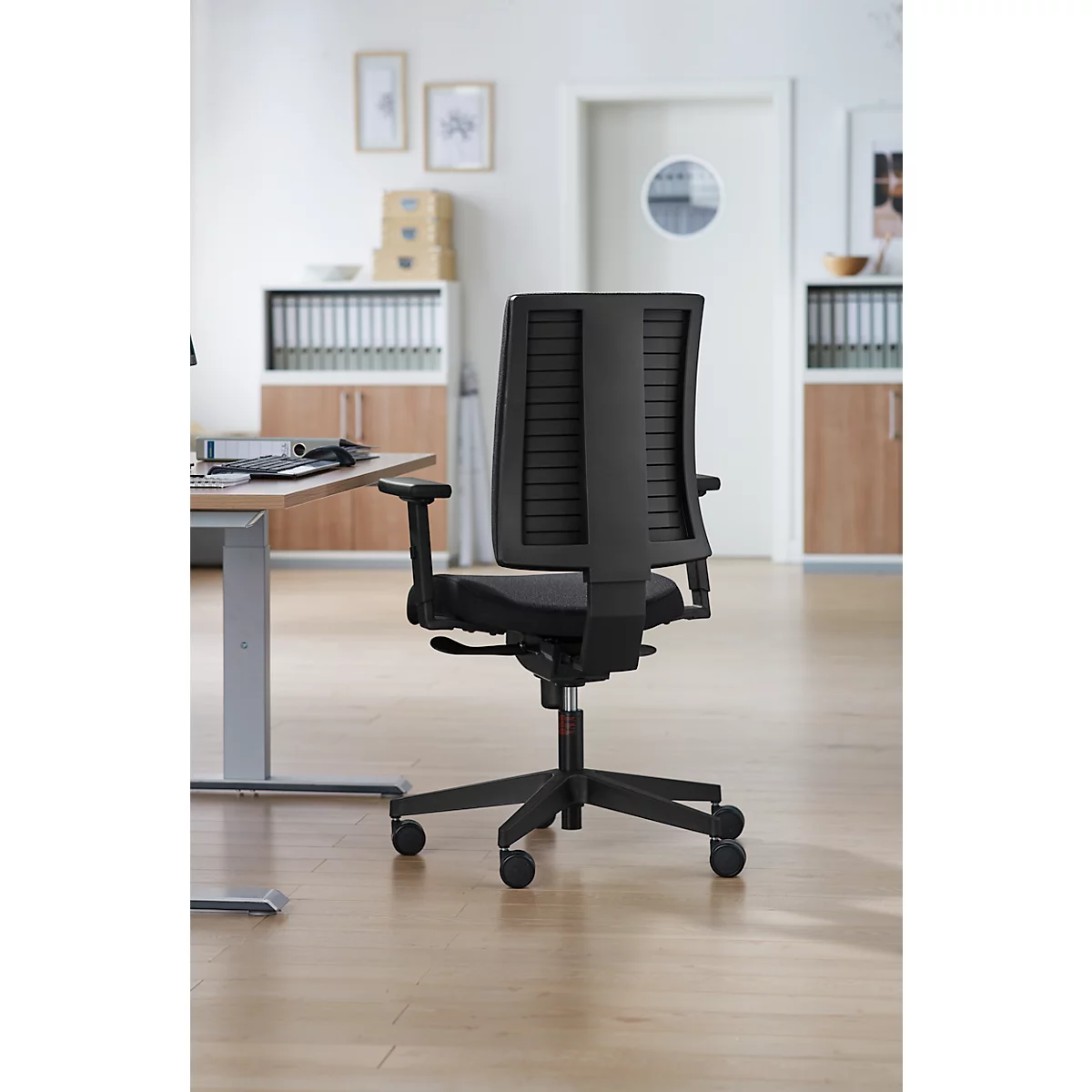 Chaise de bureau noire sur fond clair. La chaise a un dossier en maille et se trouve devant un bureau.