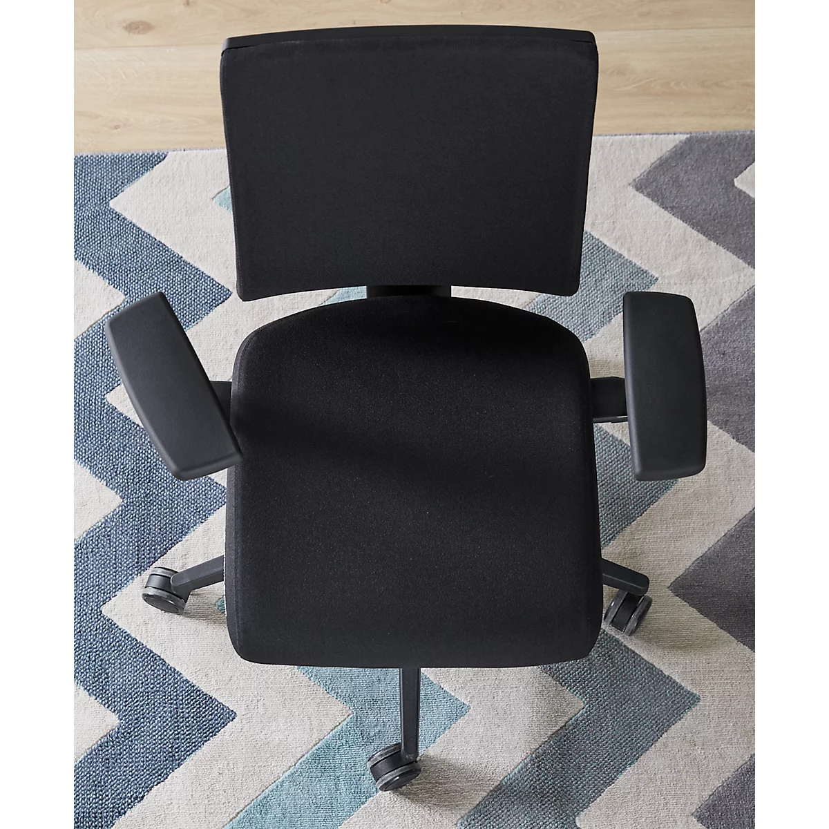 Vue de dessus d'une chaise de bureau noire avec accoudoirs. La chaise est posée sur un tapis à motif zigzag bleu et gris.