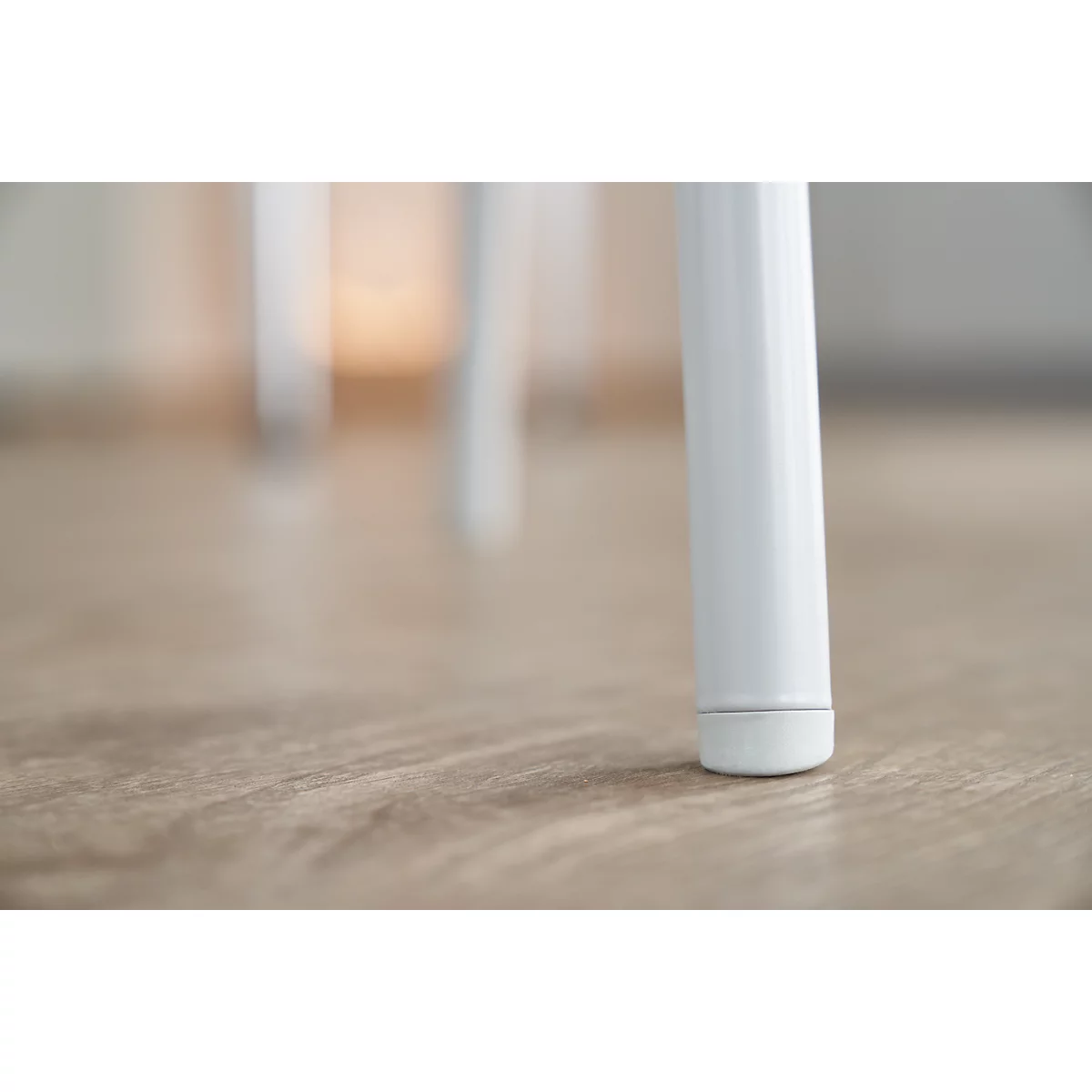 Gros plan sur un pied de chaise blanc sur un plancher en bois clair. La jambe est cylindrique avec un pied légèrement arrondi.
