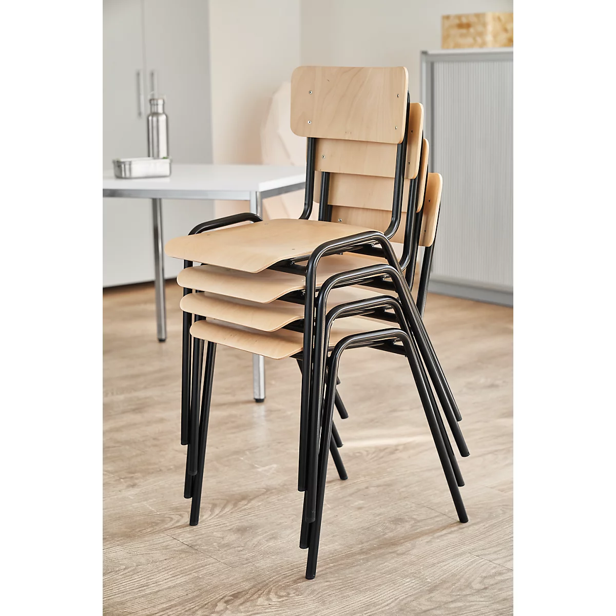 Chaises empilées avec assises et dossiers en bois, encadrées en noir, dans une pièce lumineuse.