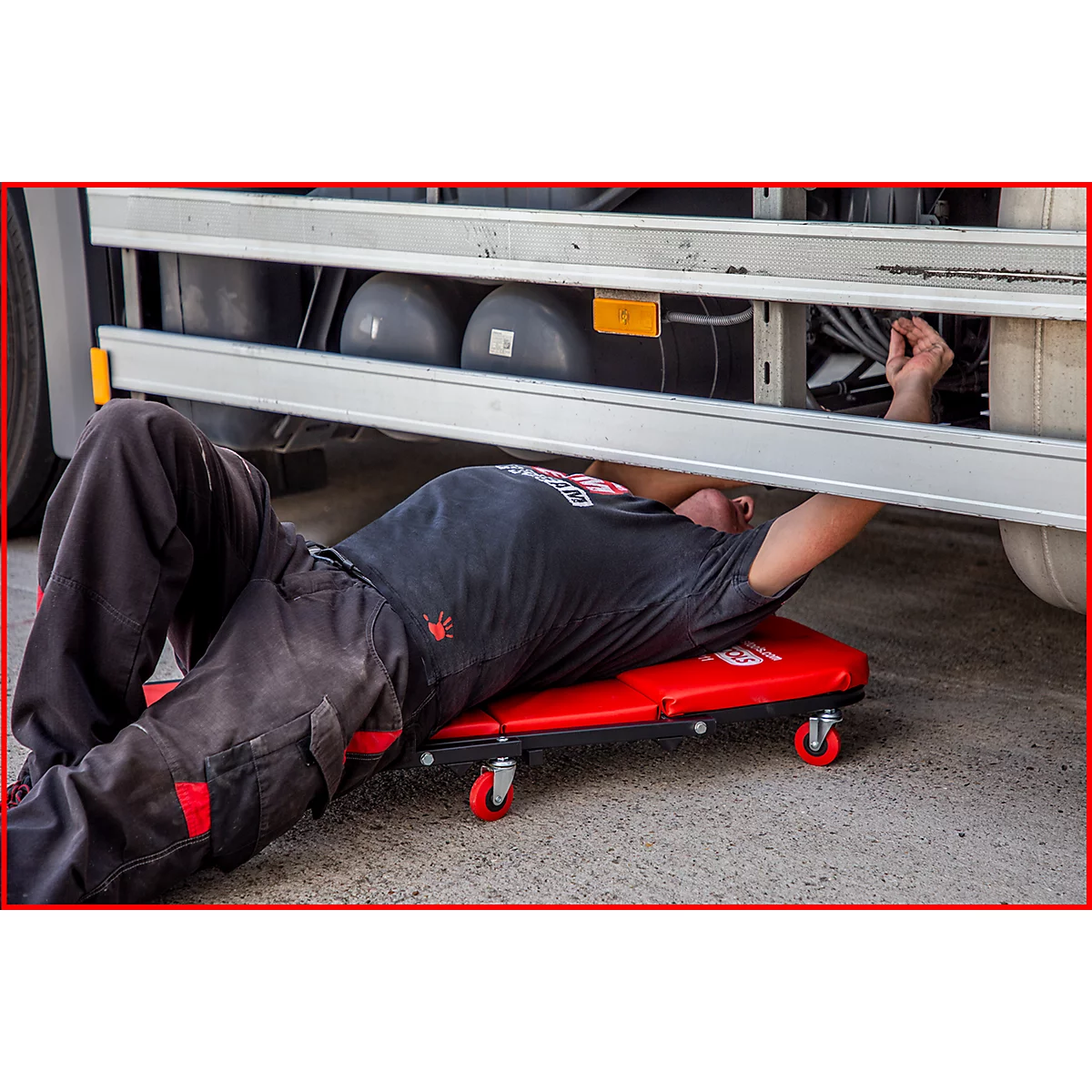 Mécanicien couché sous un camion, travaillant sur son chariot à outils rouge.