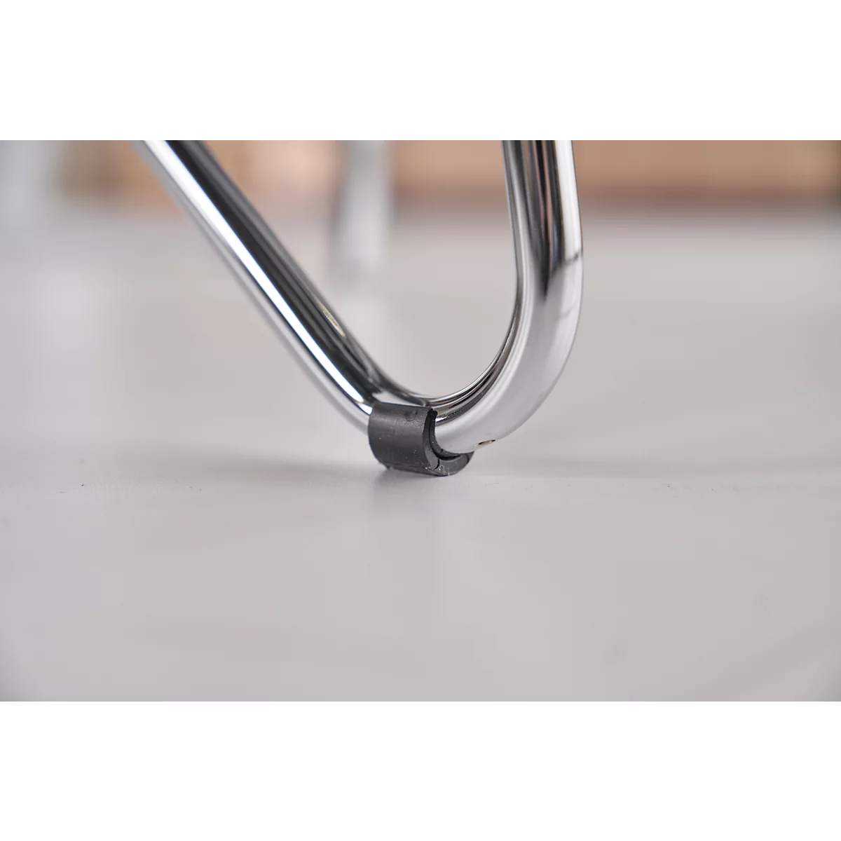 Gros plan d'un pied de chaise chromé reposant sur une surface claire. Une bague en caoutchouc noir est attachée en guise de protection.