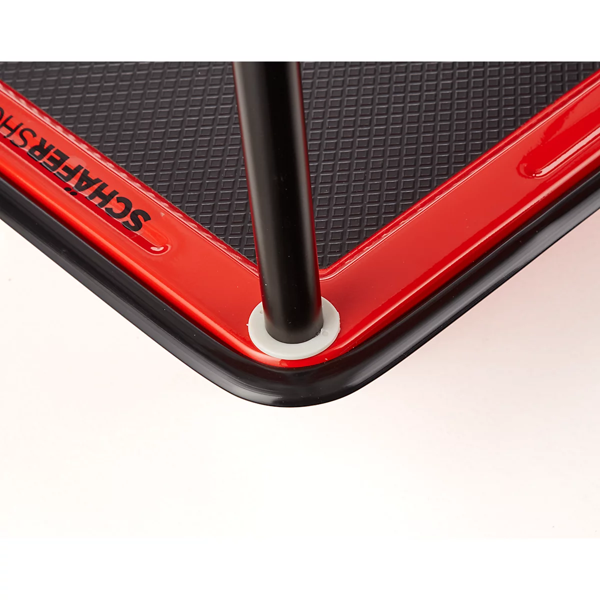 Détail d'un objet rouge, angulaire avec une surface noire et un pied en métal noir. Caoutchouc angulaire noir. Texte "SCHAFERSHOP"