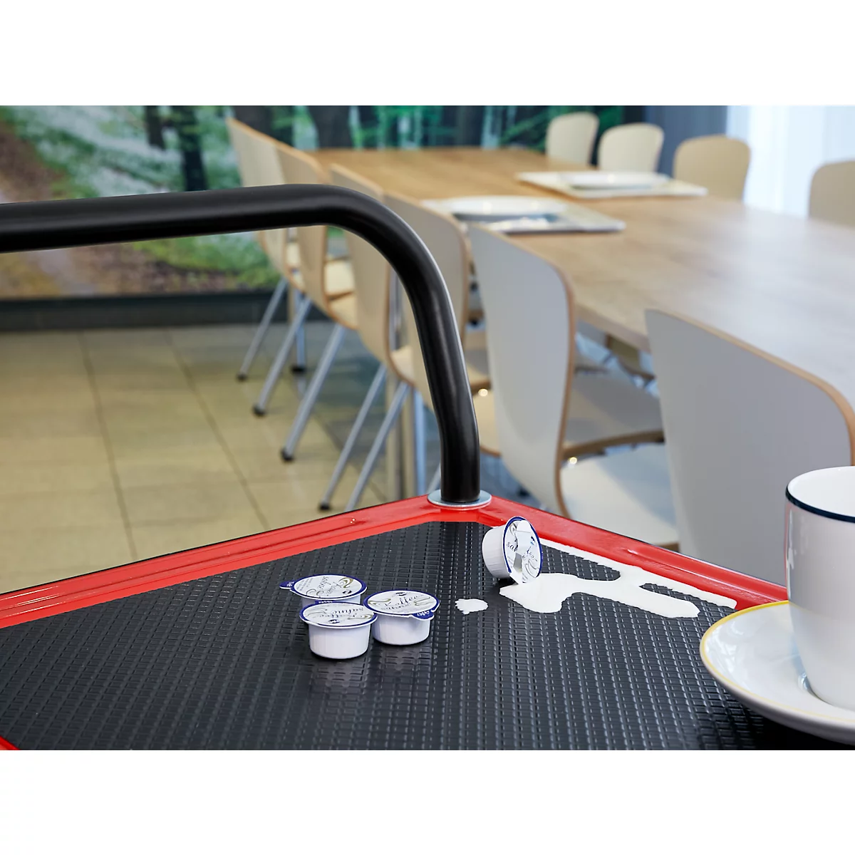 Récipients de crème à café sur un chariot rouge avec du lait renversé. En arrière-plan, une table avec des chaises.