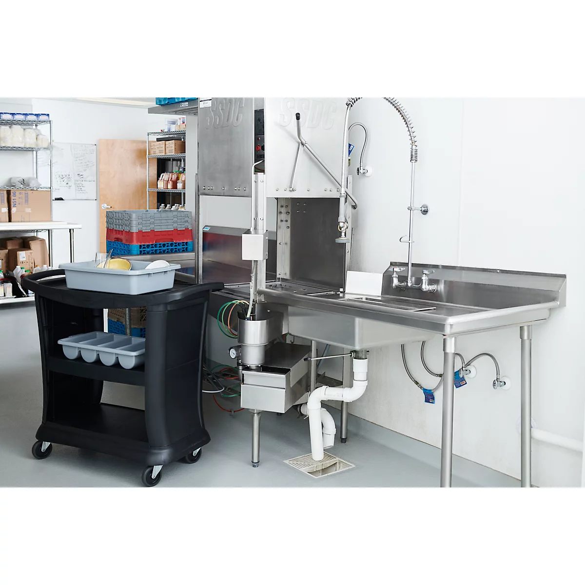 Évier industriel avec pistolet pulvérisateur, à côté d'un chariot de service noir. Le fond est une cuisine.