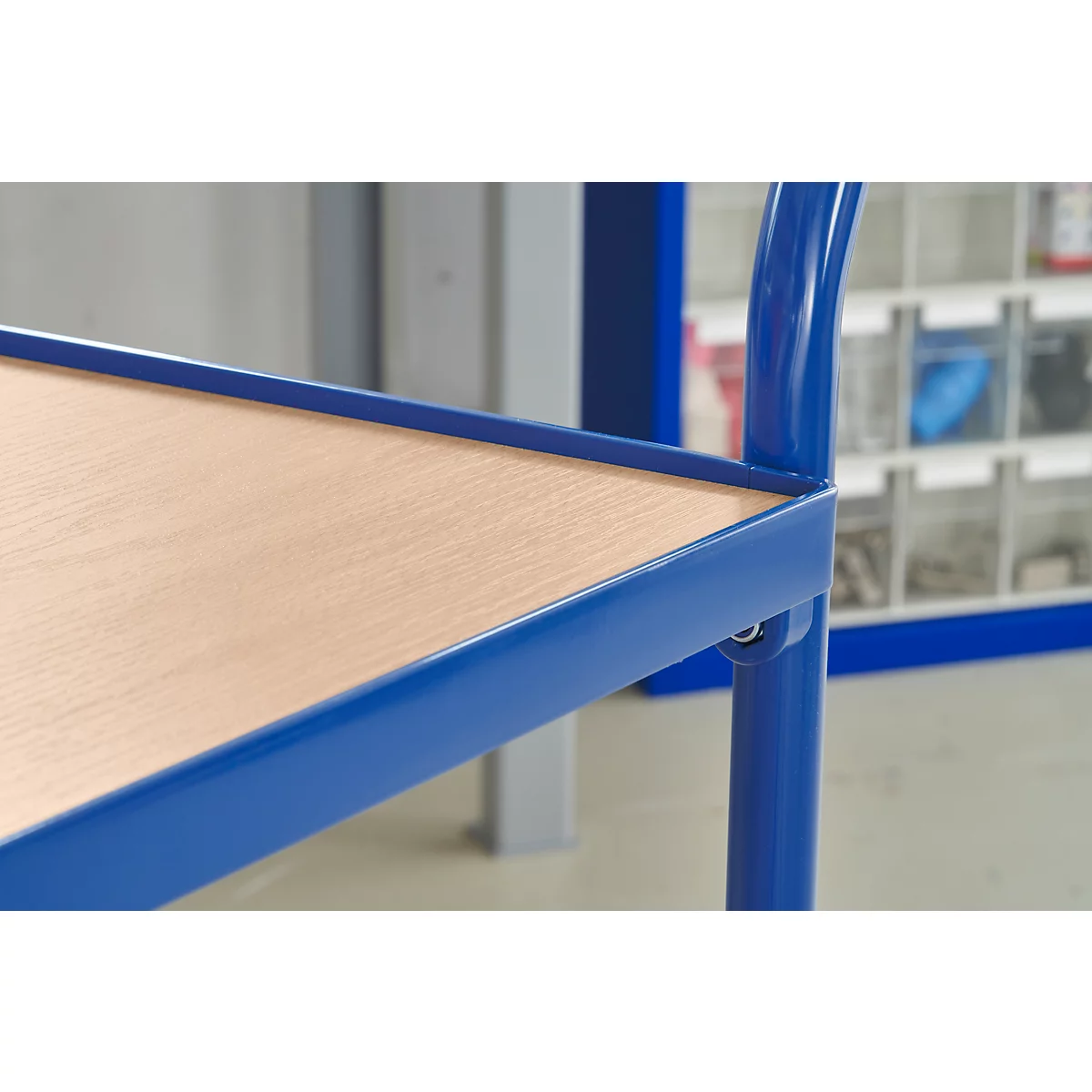 Gros plan sur une partie d'une étagère en métal bleu avec un plateau en bois. En arrière-plan, d'autres étagères sont visibles.