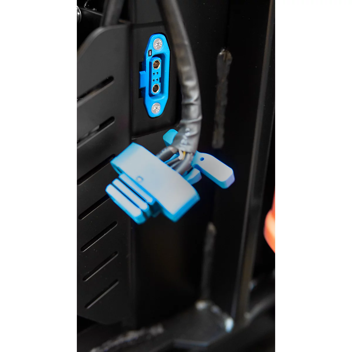 Gros plan sur des connecteurs électriques bleus fixés à une plaque métallique noire. Un faisceau de câbles sort de la plaque.