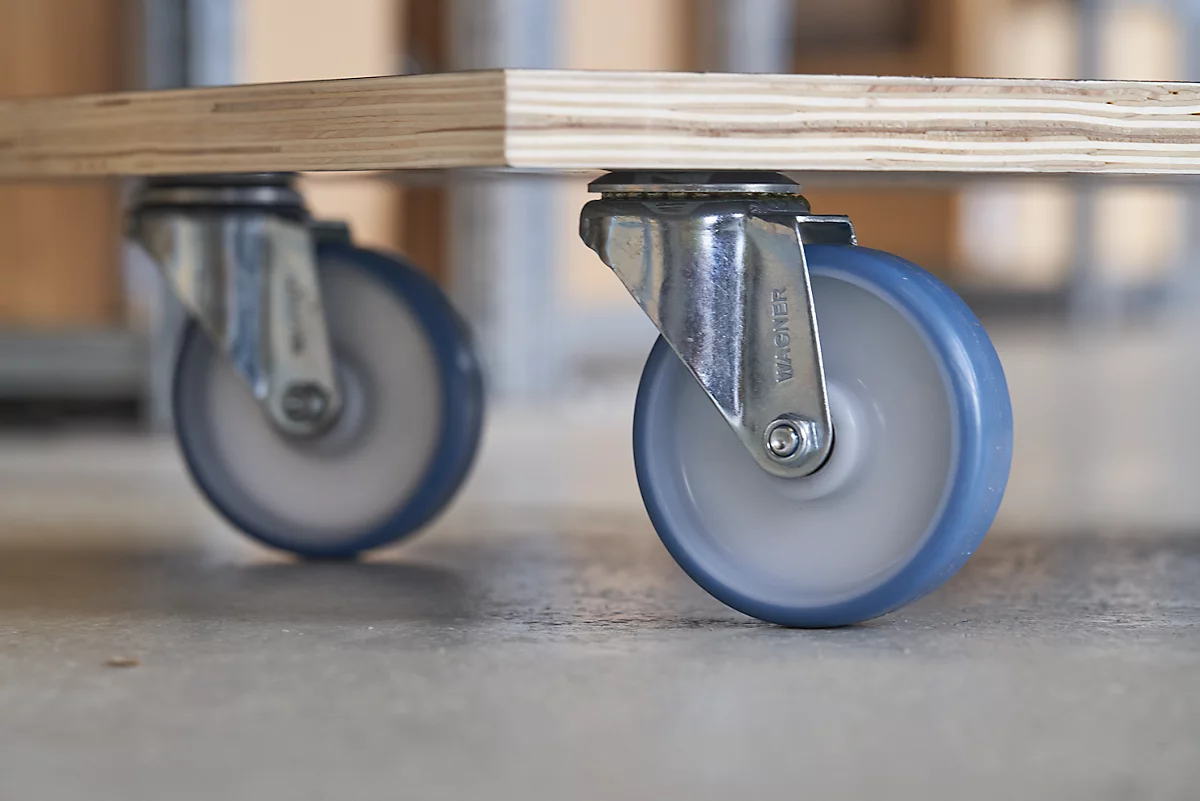 Primer plano de dos ruedas debajo de una tabla de madera. Las ruedas tienen neumáticos azules y están fijadas a marcos metálicos.
