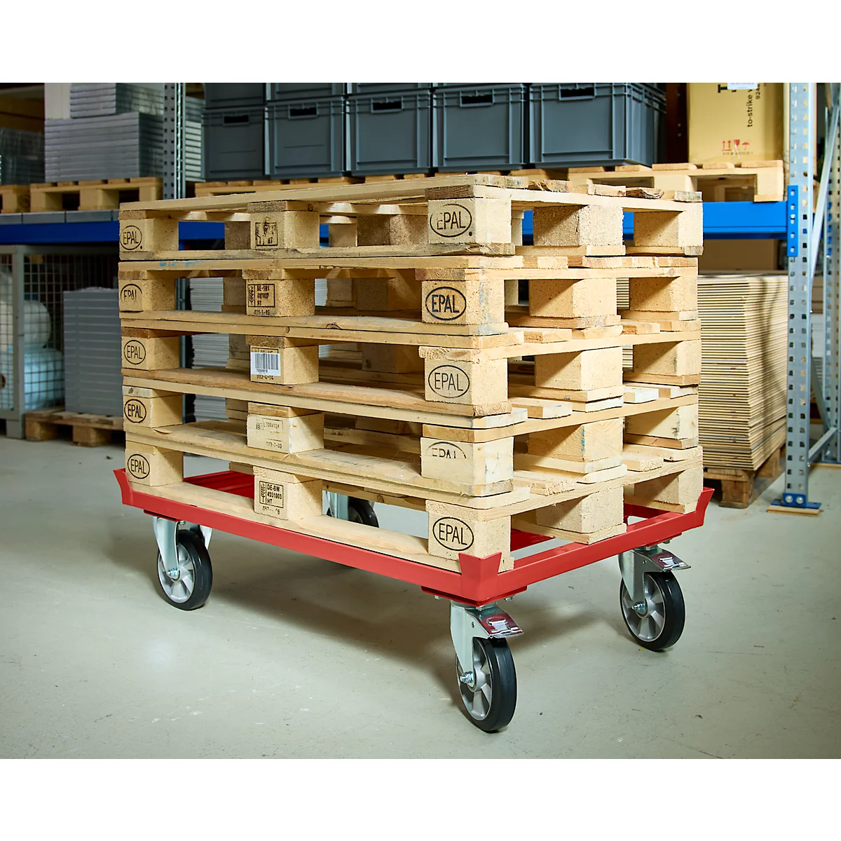 Un chariot de transport rouge avec des palettes Europe empilées se trouve sur le sol en béton d'un entrepôt.