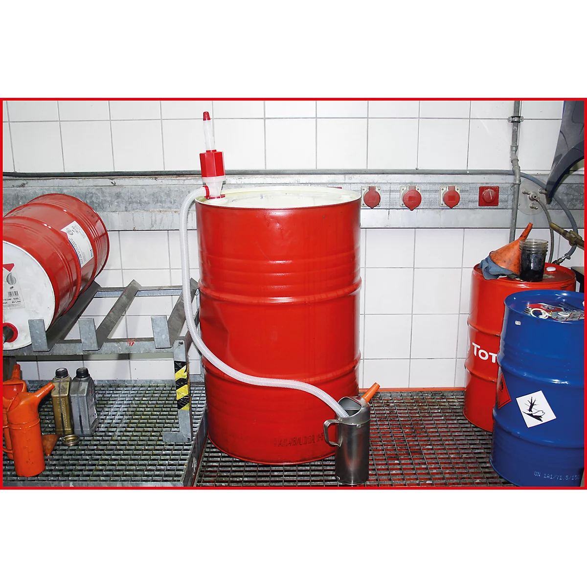 Roter Ölfass mit Pumpe und Auslauf in Metallbehälter. Weitere Fässer im Hintergrund.