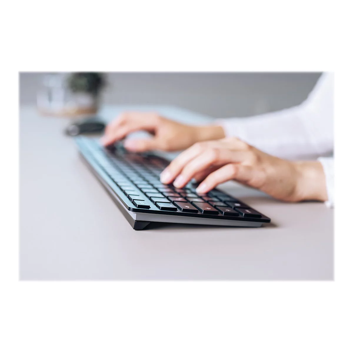 Nahaufnahme einer Person, die auf einer schwarzen Tastatur tippt. Helle Umgebung, weiße Manschette sichtbar.