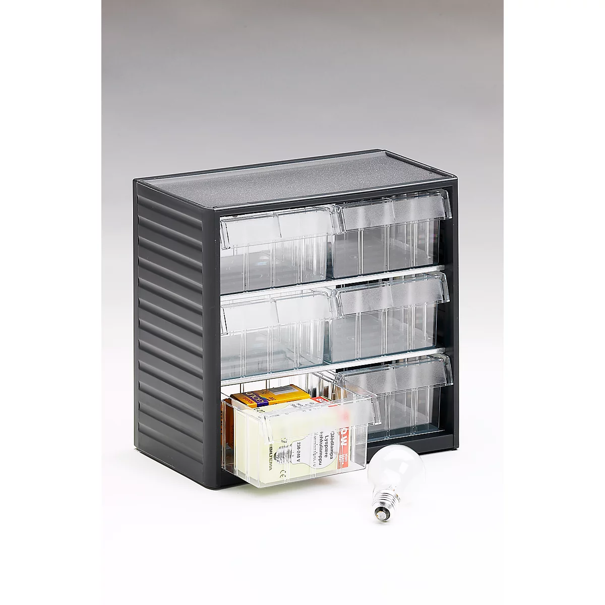 Black cabinet with three drawers. One drawer is open, filled with various items. Next to it is a light bulb.