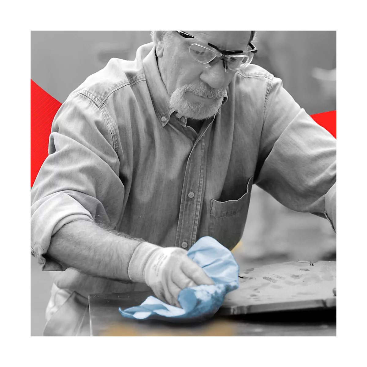 Un homme avec des lunettes et une barbe essuie une surface avec un chiffon bleu. Il porte des gants.