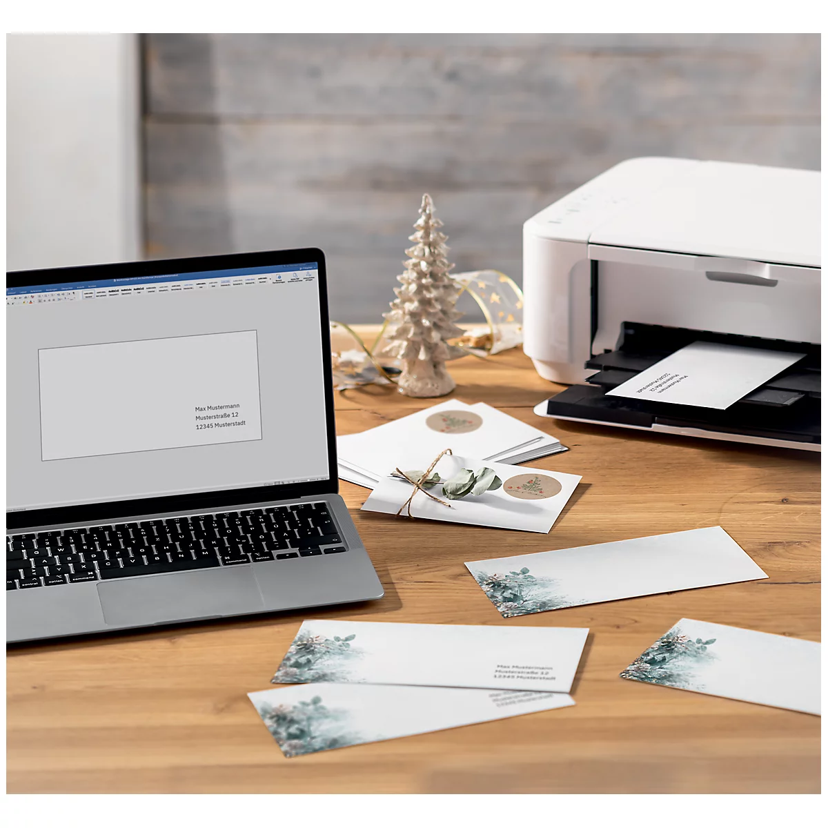 A laptop and a printer on a wooden table, with Christmas cards. The printer is printing a card.