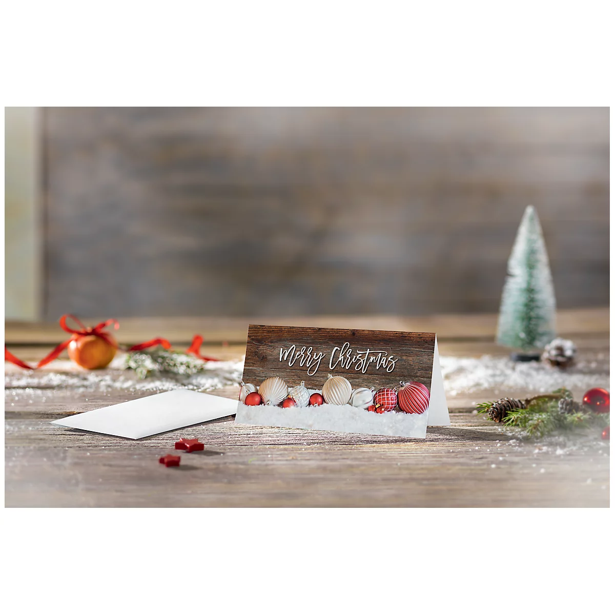 Christmas card with 'Merry Christmas' lettering on wood look. In front of it, small decorative objects in a winter landscape.