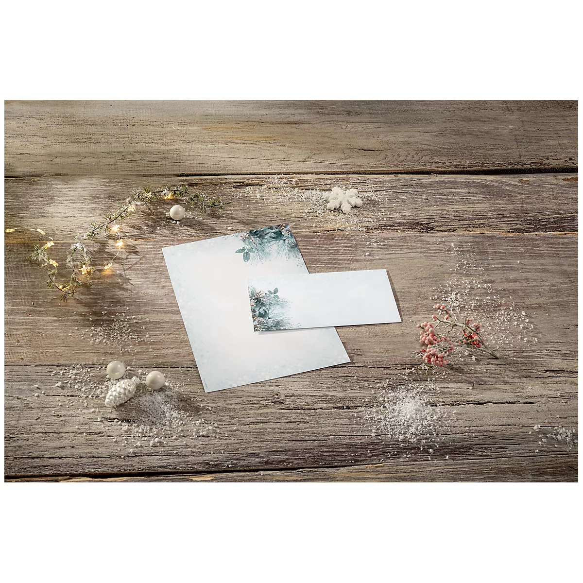 Stationery with floral patterns, card, and decor on wooden surface. Snow effect adds a winter touch.
