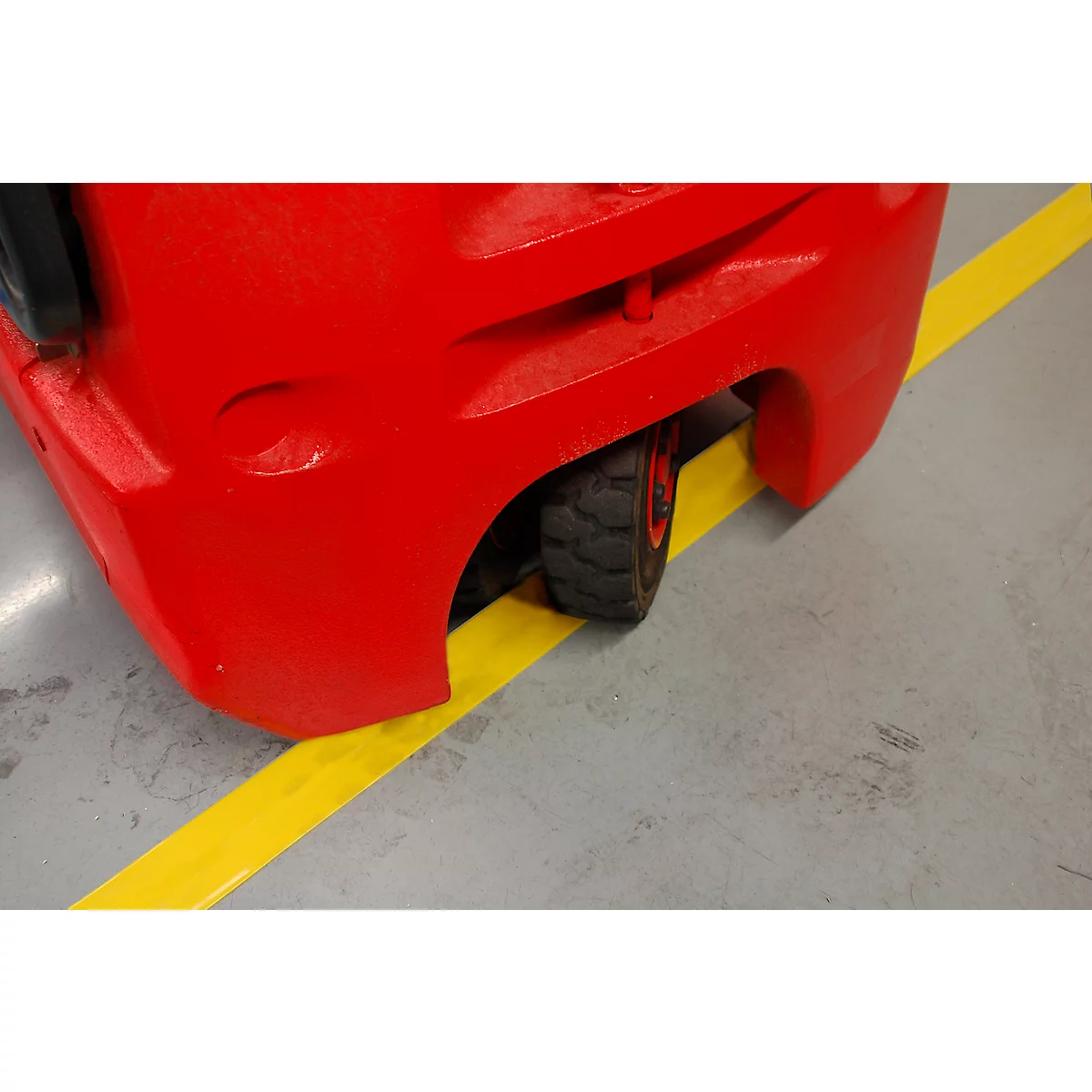 Primer plano de una rueda de carretilla elevadora roja sobre un suelo industrial gris con una línea de marcado amarilla.