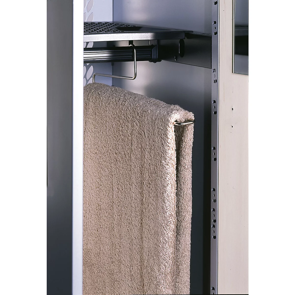 Une serviette beige est suspendue à une tringle métallique dans une armoire. Au-dessus, une étagère grillagée.