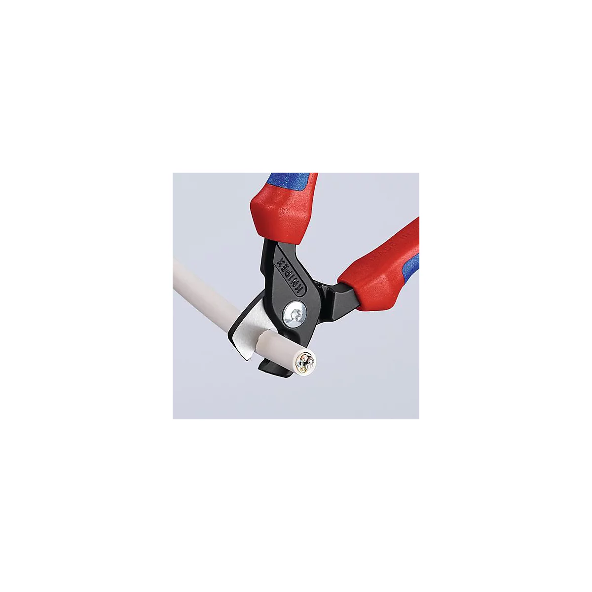 Gros plan d'une pince Knipex coupant un câble. La pince a des poignées rouges et bleues, le tranchant est noir. La gaine du câble est blanche.