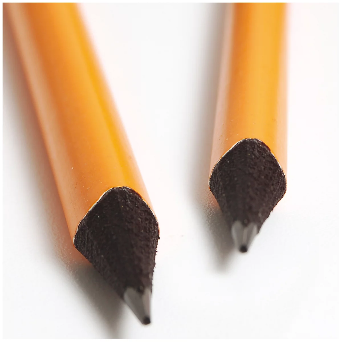 Close-up of two pencil tips lying at a light angle on a white background. The tip is made of black graphite.