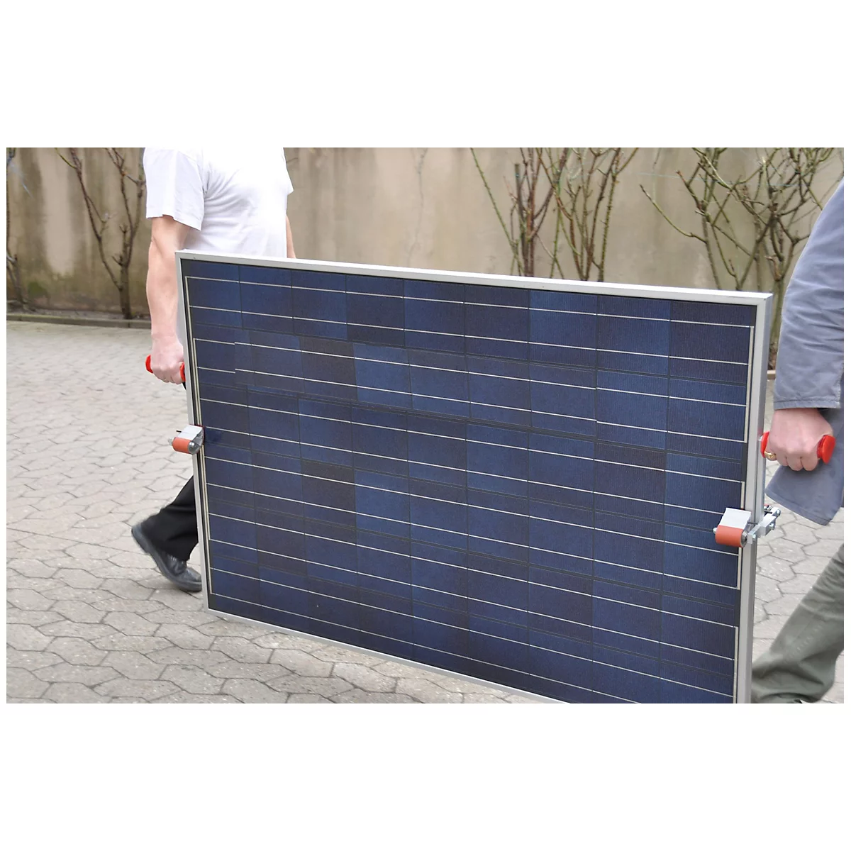 Two people carry a large solar panel made of dark blue material.