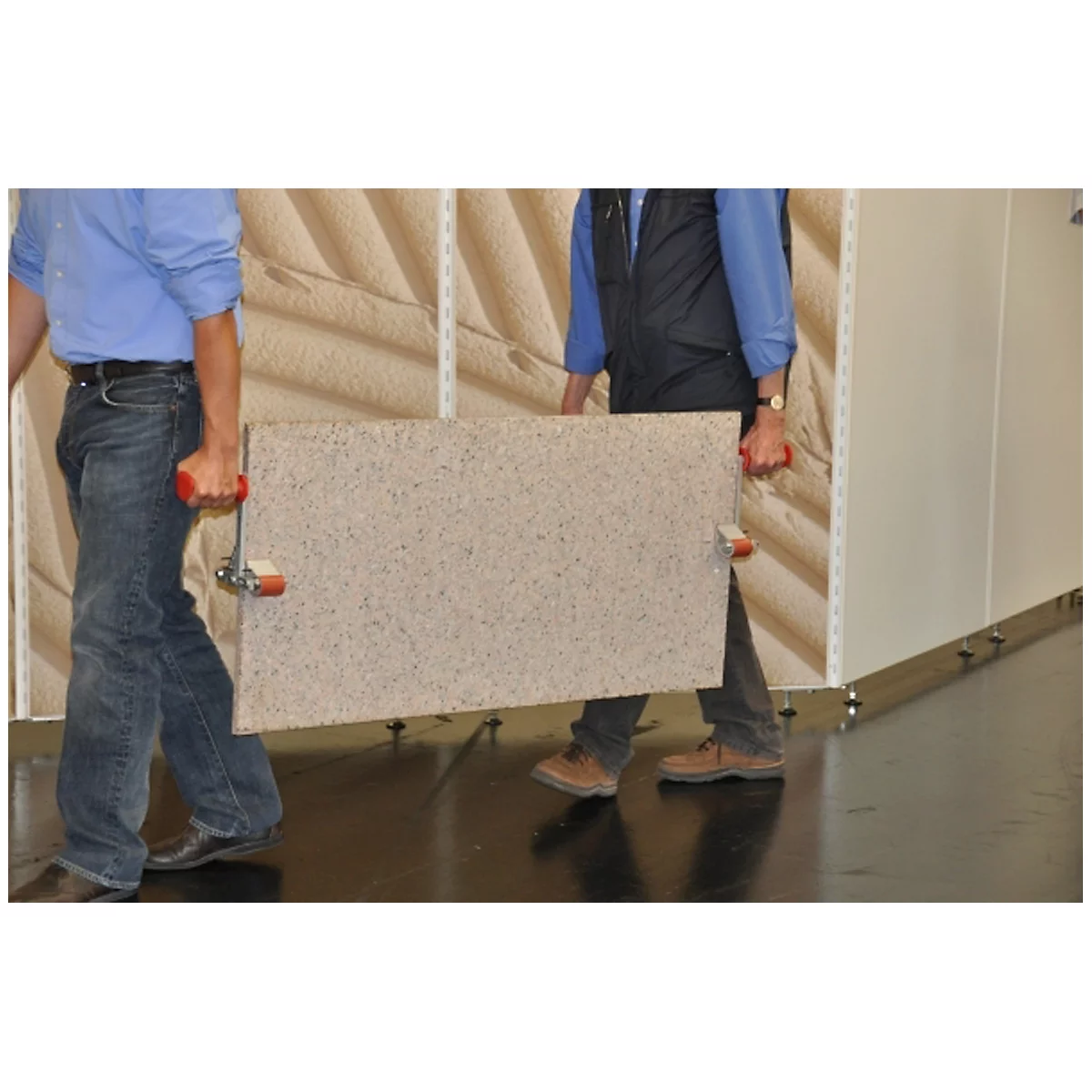 Two men are carrying a large, rectangular panel through a room.