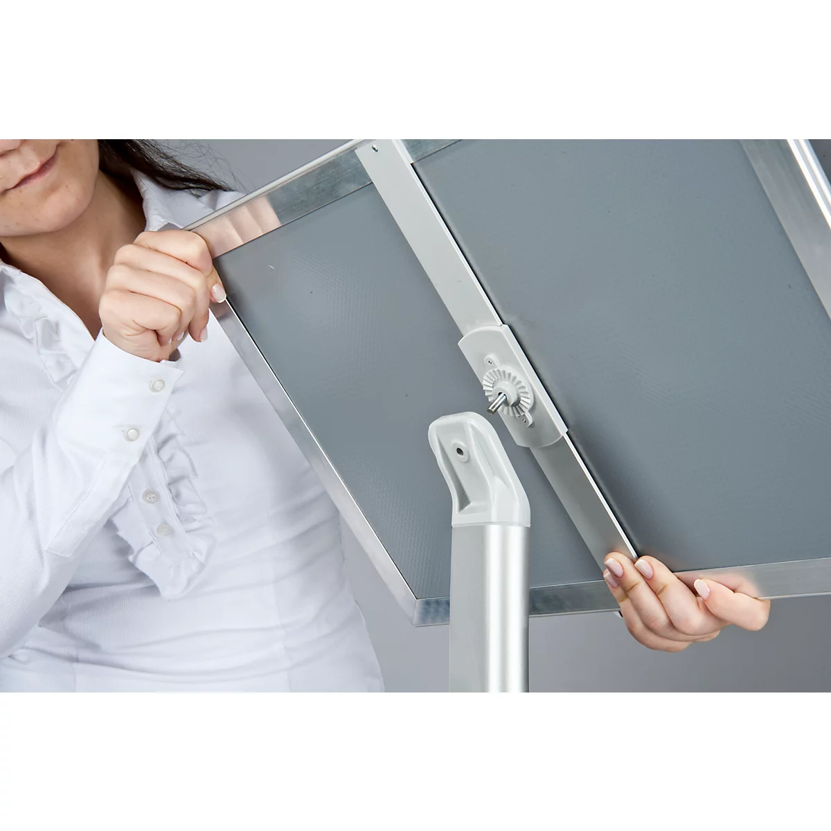 A woman adjusting a gray whiteboard on a metallic holder. She is wearing a white shirt.